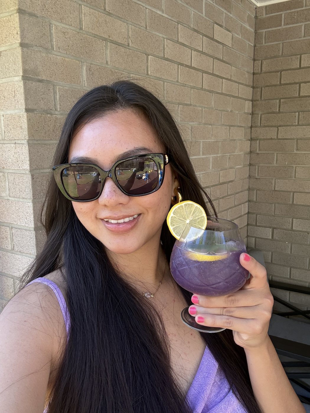 Ismriti in sunglasses holding a purple cocktail with a lemon slice