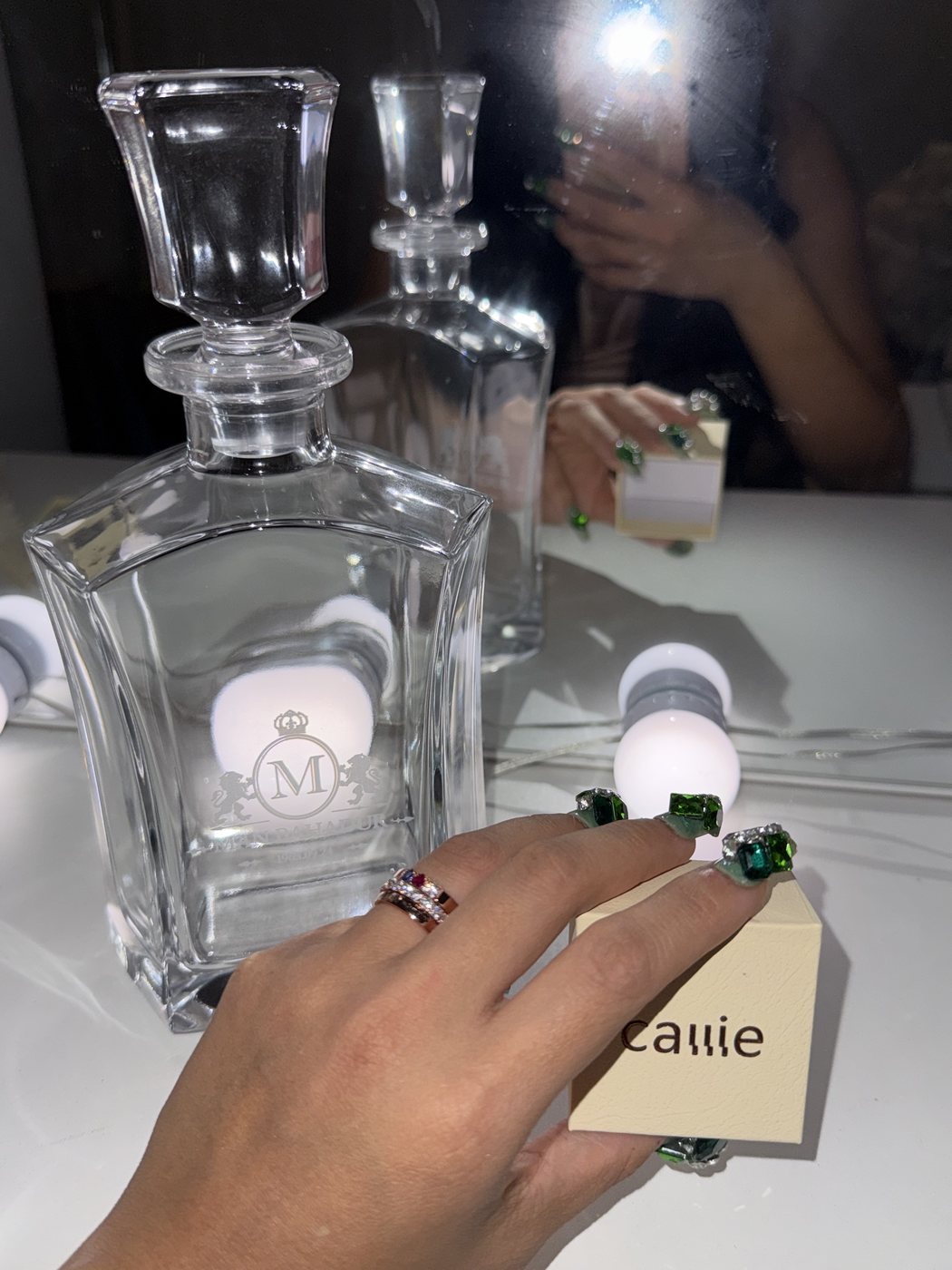 A hand holding a small perfume vial beside a crystal decanter