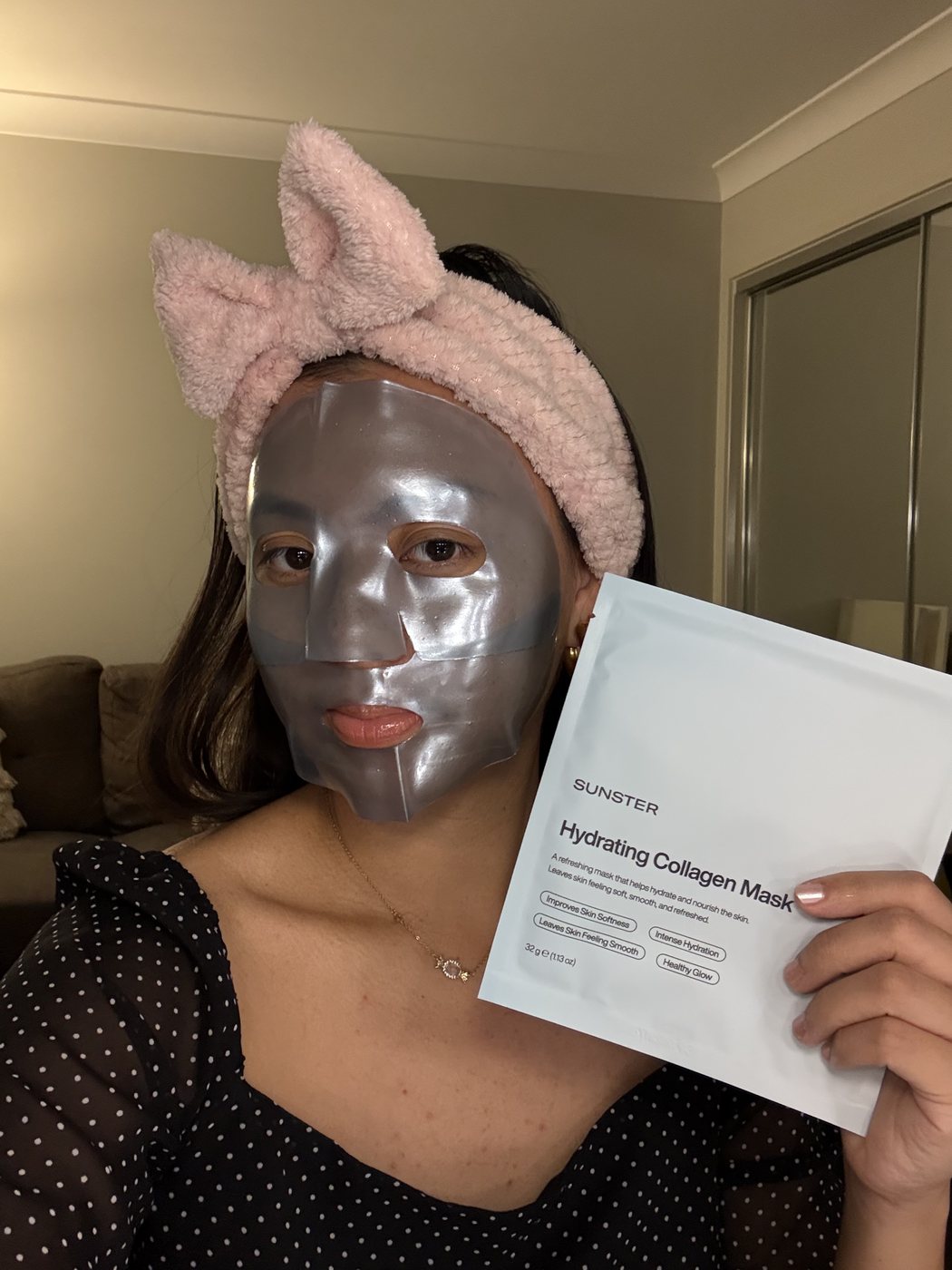 Ismriti in a pink headband wearing a silver face mask and holding the sheet mask packet
