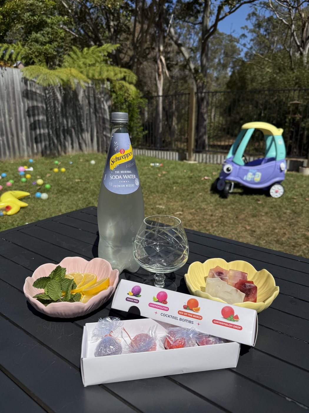 Garden table with a drink and pink flower-shaped bowls, a toy ride-on car on the lawn